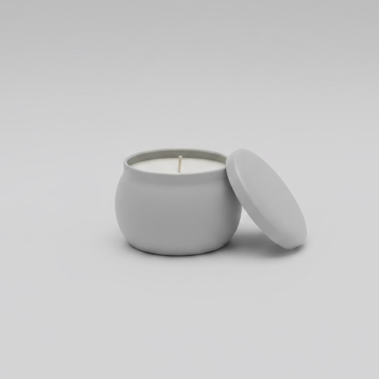 Small white candle in a tin with lid on a dark surface, with a store interior in the background.