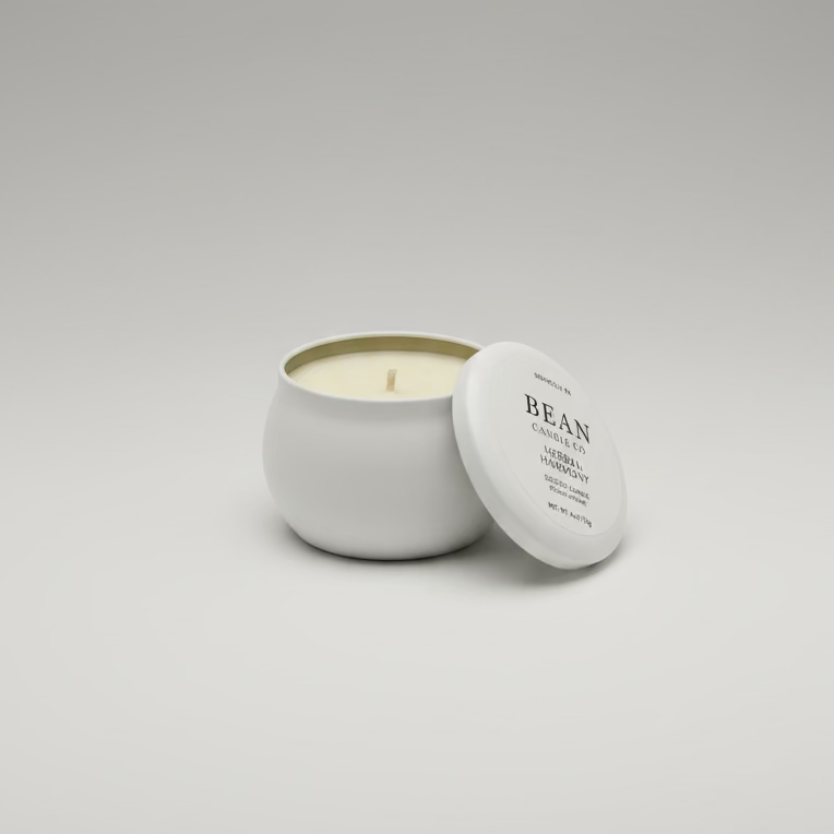 Small candle in a tin with lid on a wooden surface, possibly in a cafe setting.