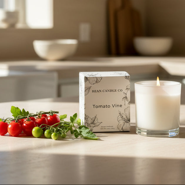 Candle and packaging labeled 'Tomato Vine' from Bean Candle Co. on a kitchen counter with tomatoes and leaves.